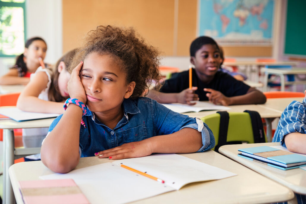 young child looking distracted and unhappy in classroom at desk with ADHD