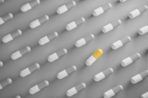 various white and grey pill capsules with a yellow and white one in the middle