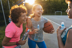 mom and kids laughing while drinking water on basketball court