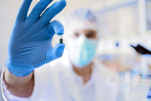 masked lab technician holding medication up in gloved hand