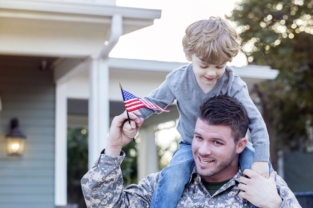 veteran holding child on shoulders with american flag