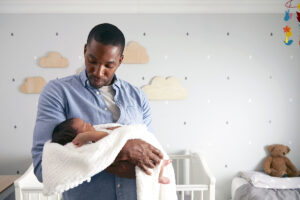 father holding baby next to crib