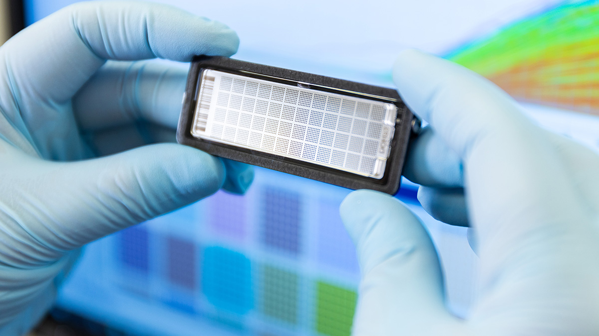 Genomind lab dna sample panel held up by two hands wearing blue gloves in front of computer with rainbow data