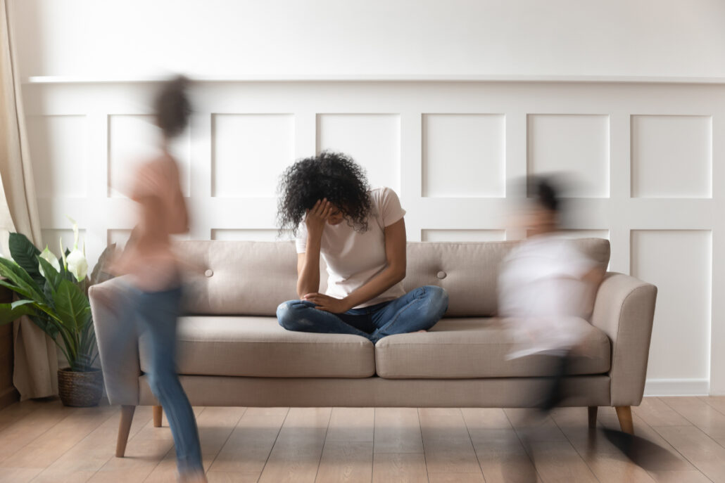 woman sitting on couch upset while children run around house