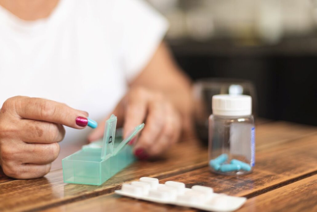 woman placing blue pill capsules in pill container