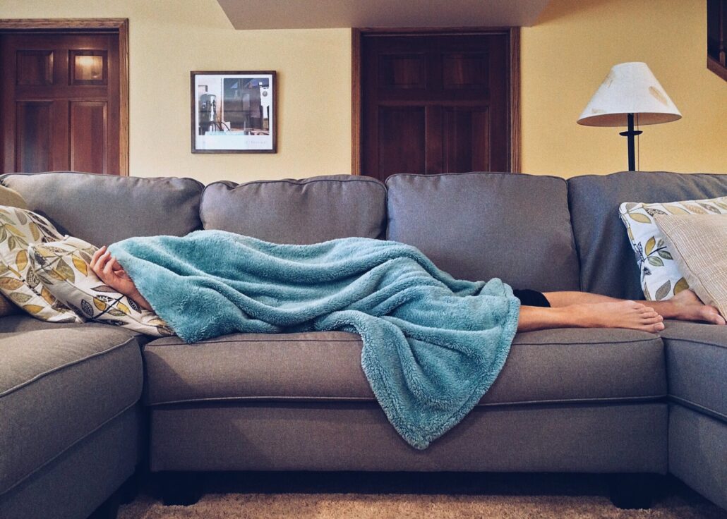 person sleeping on couch with blue blanket