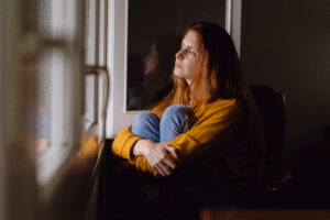 young woman looking pensively out a window sitting